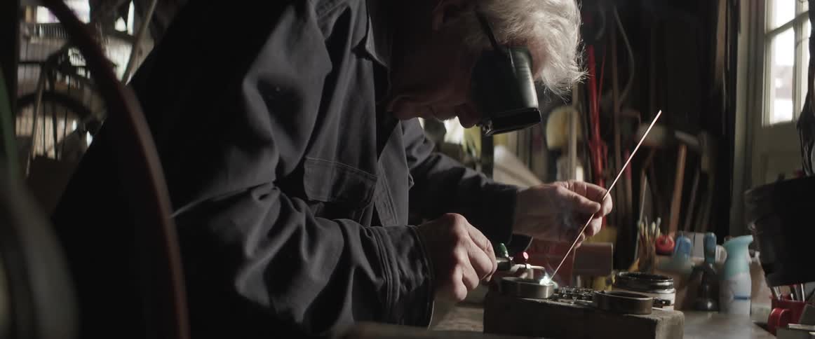 An old man uses a torch on a piece of metal