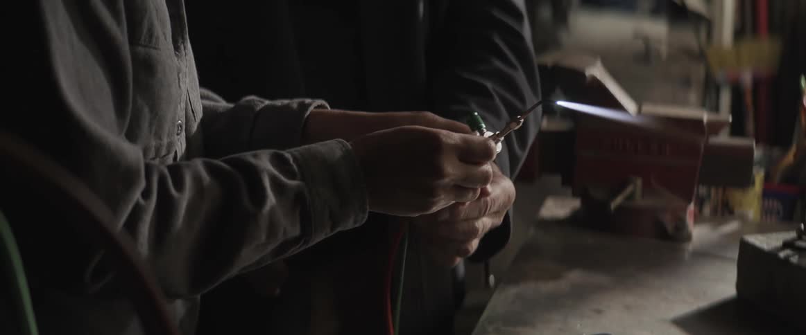 A man helps a younger woman learn to use a small torch