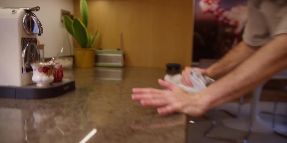 A man wipes down a kitchen counter while playfully dancing as he cleans