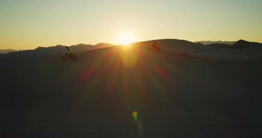 Two people ride motorbikes across a desert