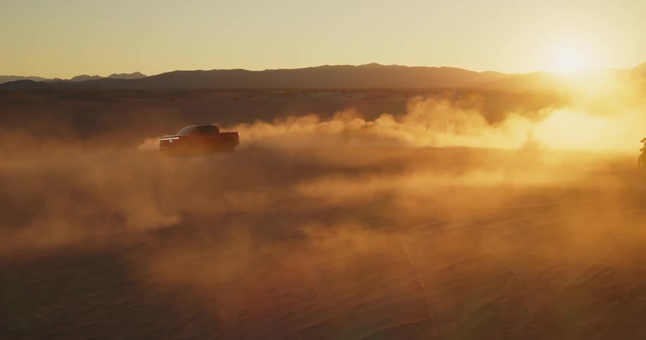 Pickup truck and motorcycles driving in circles over desertcreate clouds of dust at sunset