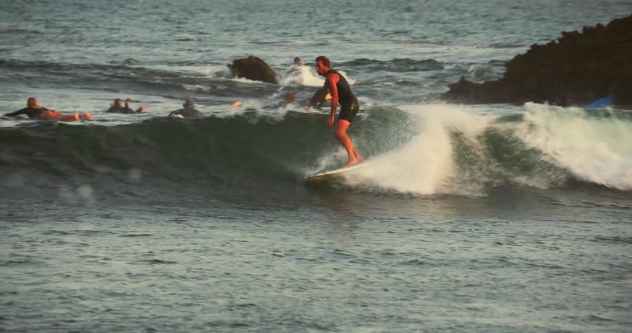 From a group of surfers one catches a small wave and rides it until he almost falls