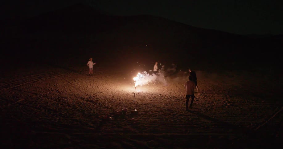Group of friends on the sand at night lighting fireworks
