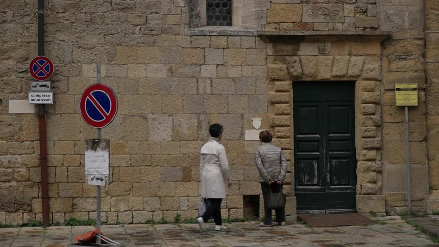 An elderly couple walks up to and reads a sign on a stone wall