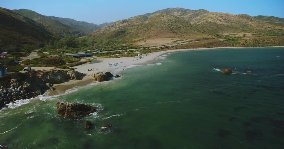 Vehicles drive along roads near beach bordered by mountains