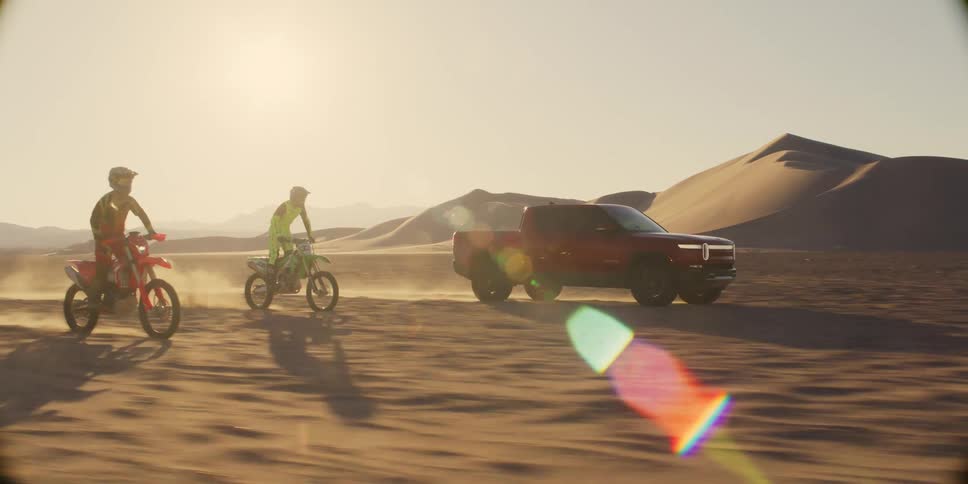 Two motorcycles doing motocross next to a pickup truck in a desert