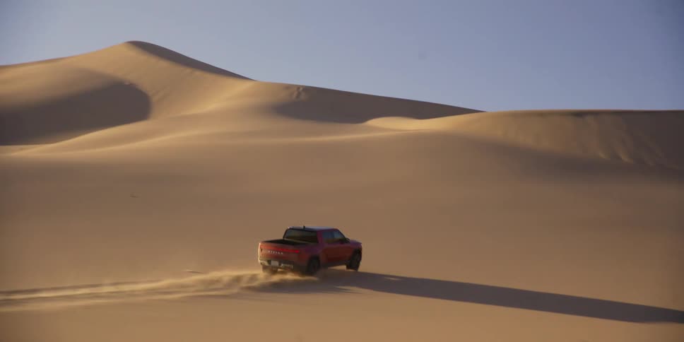 A red pickup truck is skidding on the sands of a desert with several dunes
