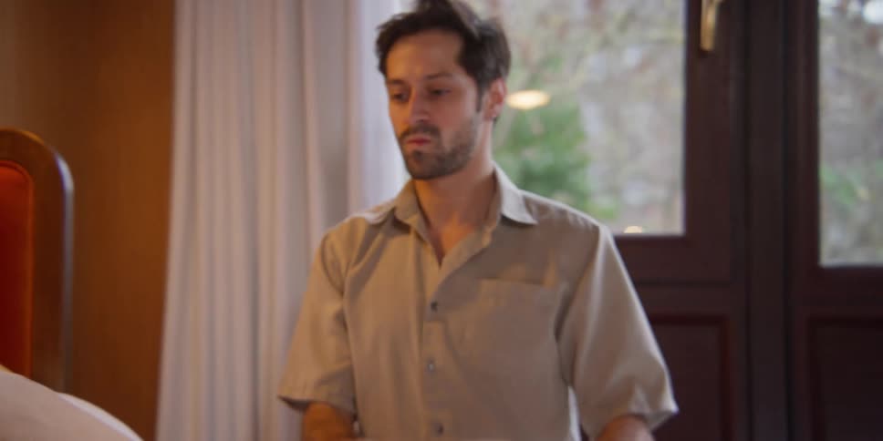 A man plumps pillows and then collapses onto the bed