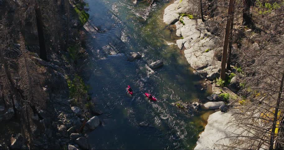 View from above of two people in separate canoes traveling along a river in the middle of the forest