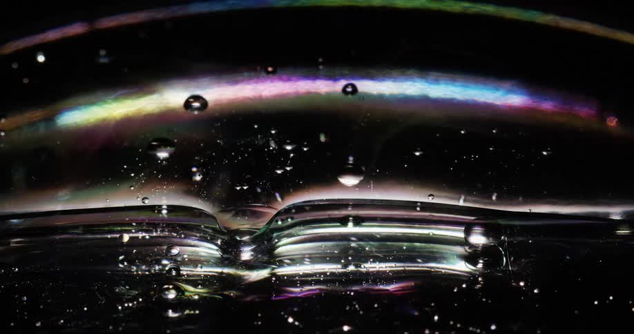 A closeup of an oily dark bubble with a spectrum of colors reflecting on its surface