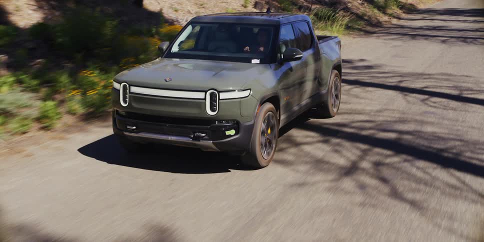 A gray pickup truck is driving on a rural street and pulls into a forest with dry trees