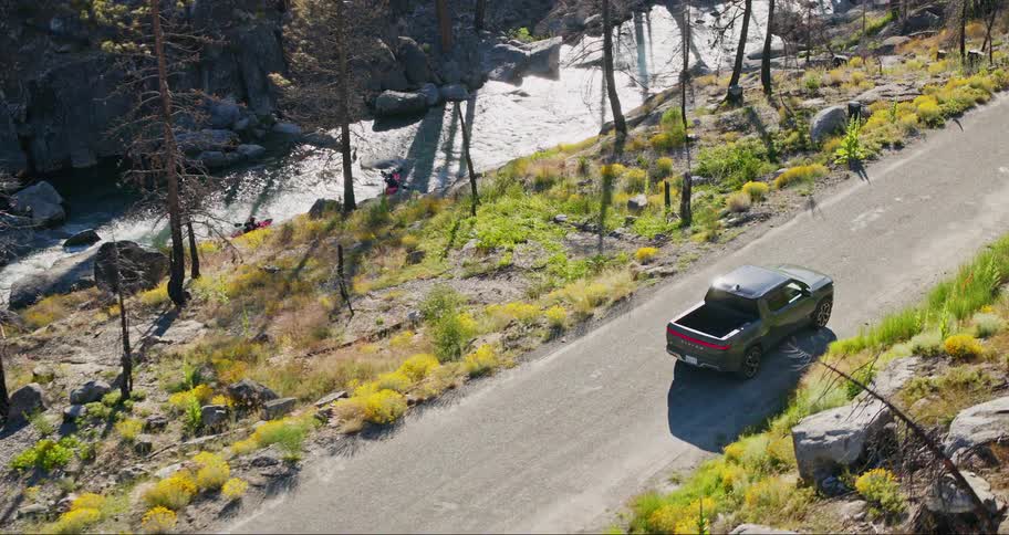 A pickup truck on a forest road driving parallel to two people going down a river in canoes