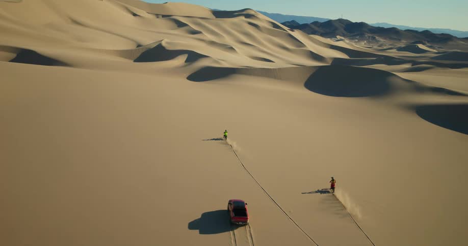A truck and two motorcycles ride through a desert