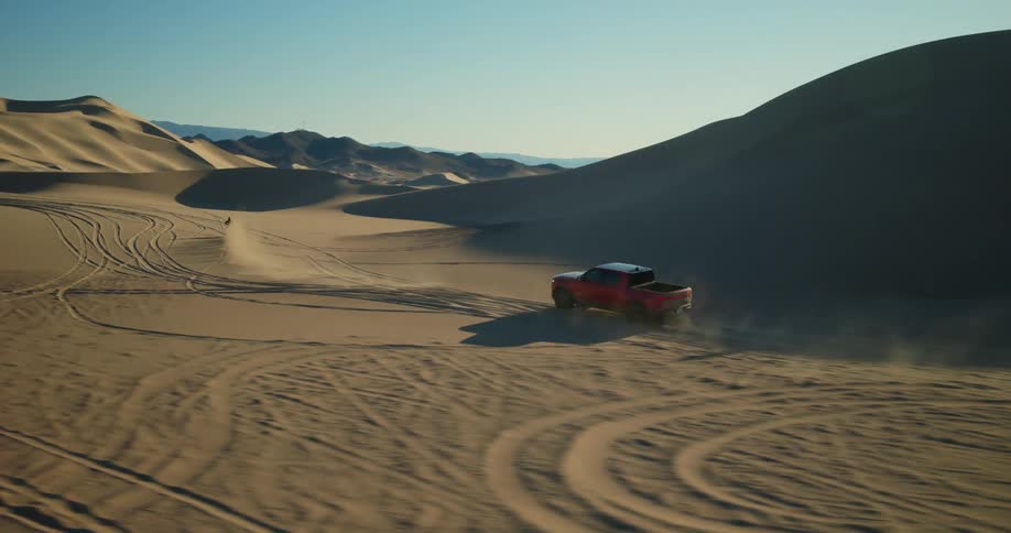 A group of people riding dirt bikes and driving a truck in the dunes