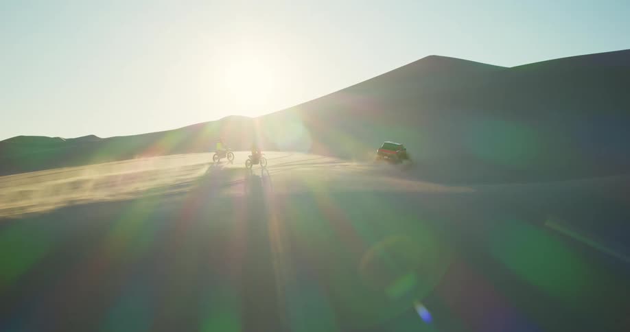 A truck and two motorcycles drive in a desert
