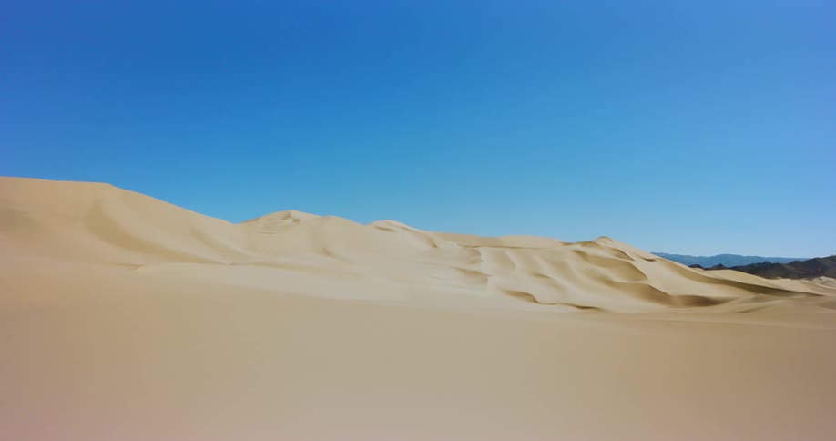 Yellow sand of desert contrasts with bright blue of sky and green mountains on horizon