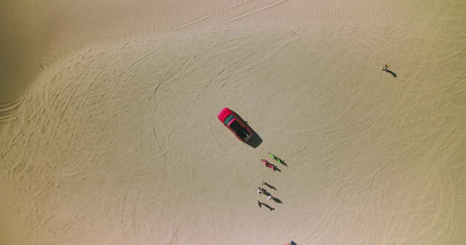 An aerial view of a group of people near a red car over a sand dune