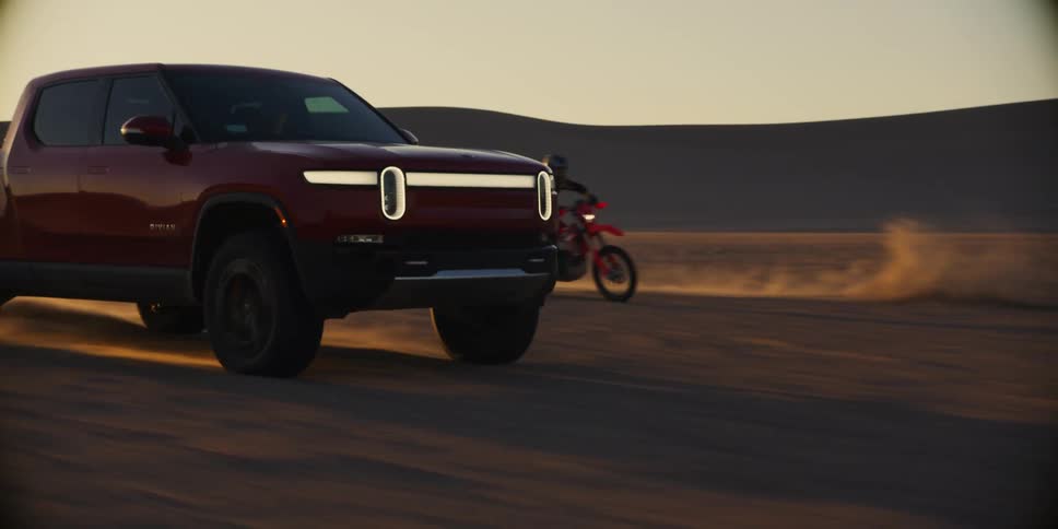 A red pickup truck and two motorbikes driving in a sandy desert and raising a lot of dust behind them