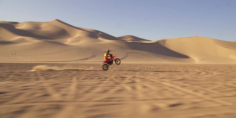 Two people doing motocross in a desert region with several sand dunes