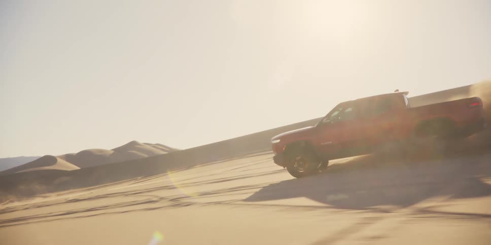 Large red vehicle next to a motocross moving through the desert sands