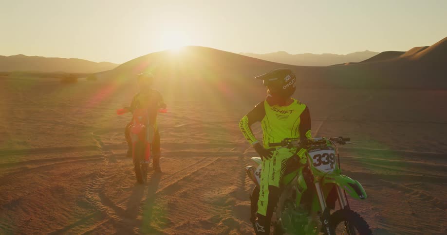 Two motocross sportsmen next to a red pickup truck in the middle of the desert that