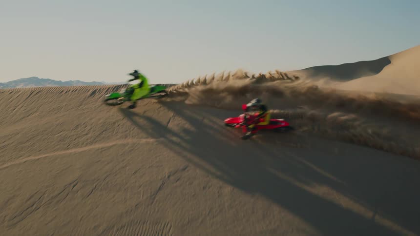 Two people with their motorcycles making a turn over a dune in the desert