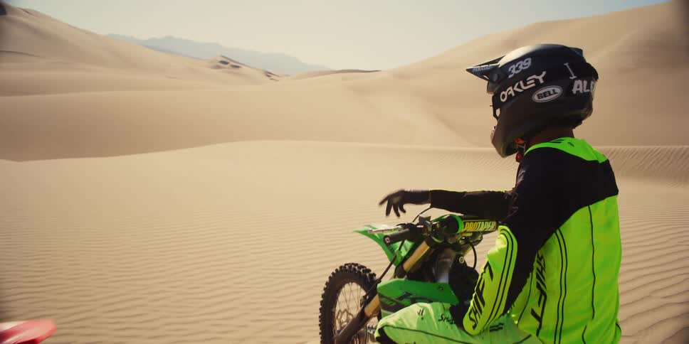 Two motorcyclists sit on bikes in desert talking on a sunny day