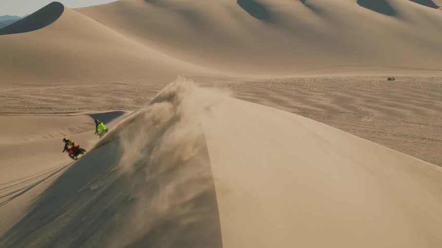Two people doing motocross are climbing a huge sand dune in the desert