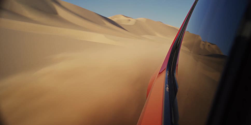 The exterior bodywork of a car driving in the sand of a desert and throwing sand into the air
