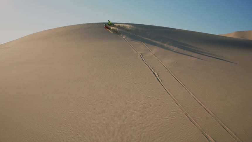 Two people doing motocross up a sand dune in the desert