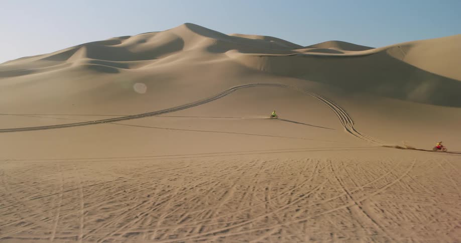 Two people doing motocross in a desert with some dunes behind