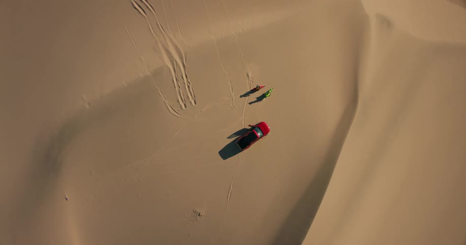 View from above of two motorcycles and suv in the middle of a desert dune