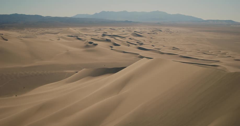 Aerial view of sand dunes in the desert next to the mountains