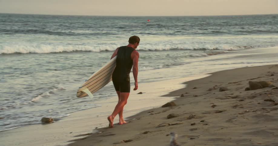 Man walking on the sea sand with his surfboard and all wet