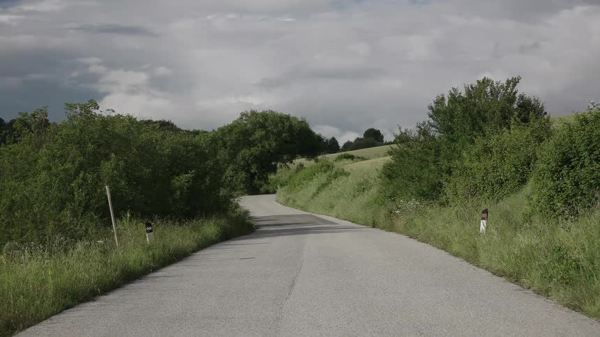 A country road that is winding and surrounded by brush and trees