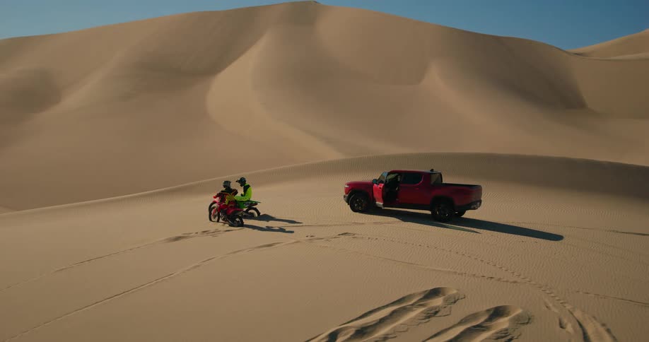 A clip of two persons on a motorbike parked beside a red truck in the desert