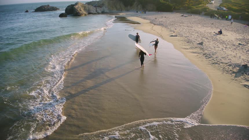 Three surfers walking along the beach with their boards