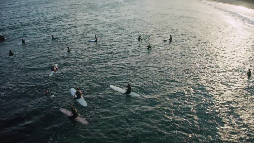 A group of surfers waits in the water near a rocky beach with a building on top