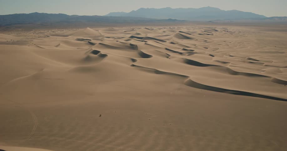 A desert region with several sand dunes and in the background there are large mountains on the horizon