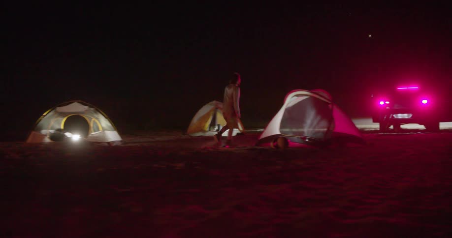 Several people camped in a desert and there is a motorcycle and a car parked