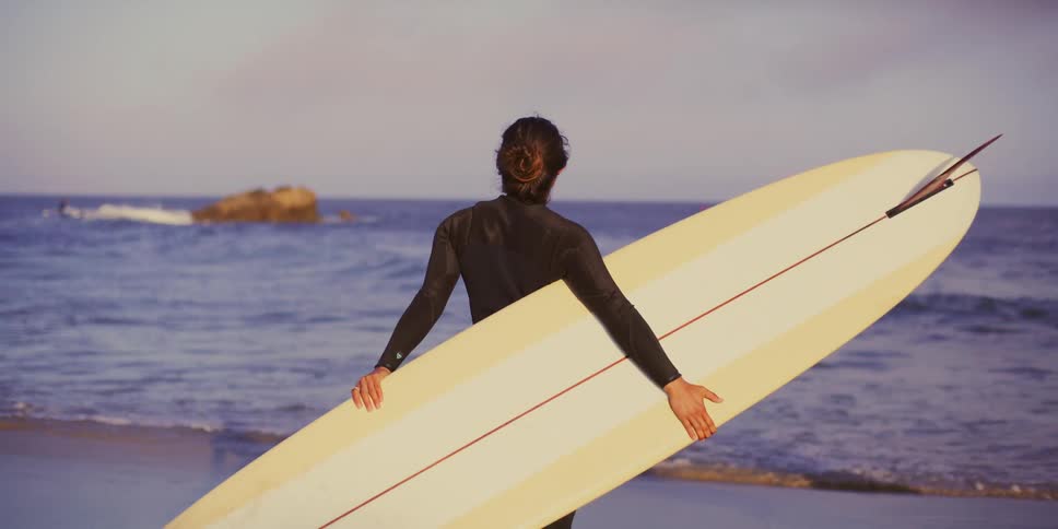 Surfer woman in the arena in front of the sea holding her long board