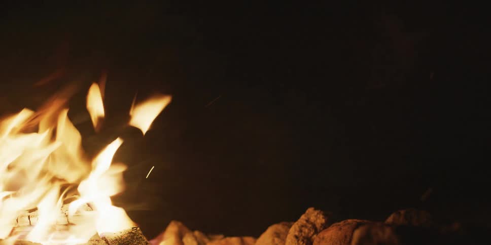 Closeup of a bonfire releasing embers and smoke at night