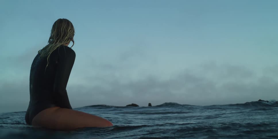 A clip of a lady sitting on a surfboard in the water