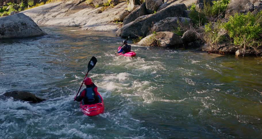 Two people kayaking on a river with lots of rocks and the kayaks are red