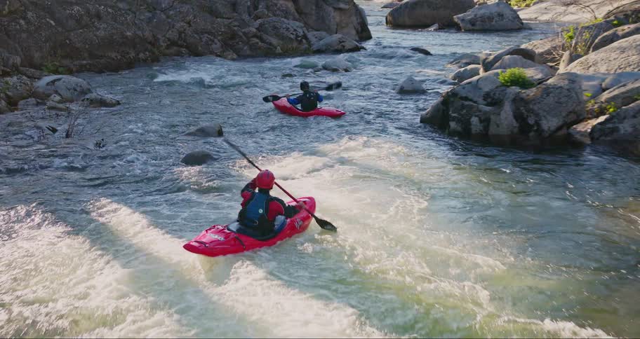 Two people in different canoes canoeing down the river in a forest