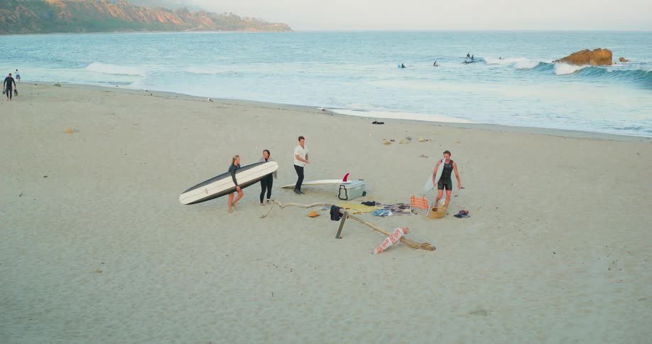 Surfers walk across beach and set surfboards down near their towels