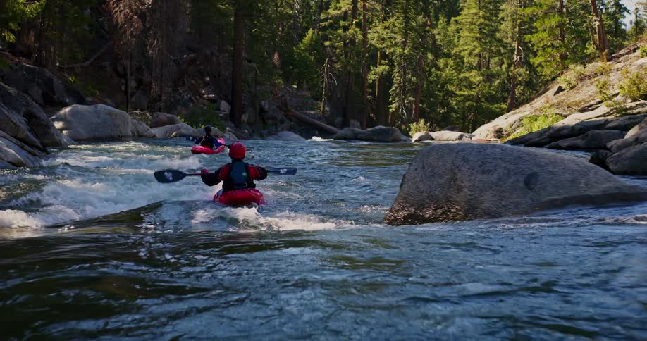 Two people going down a river using red kayaks and there are many rocks in the river