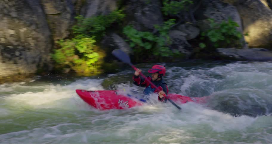 A person wearing a safety helmet is kayaking on a river and makes a small fall