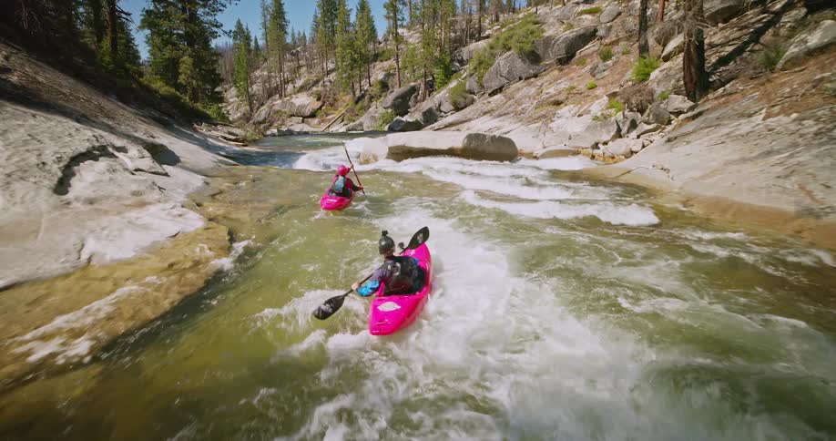 Two people in pink kayaks are going down a river that passes through many rocks