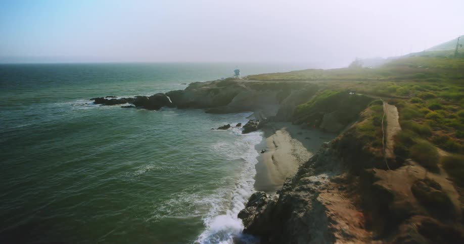 A rocky coastline with waves crashing against the rocks next to green grassy fields